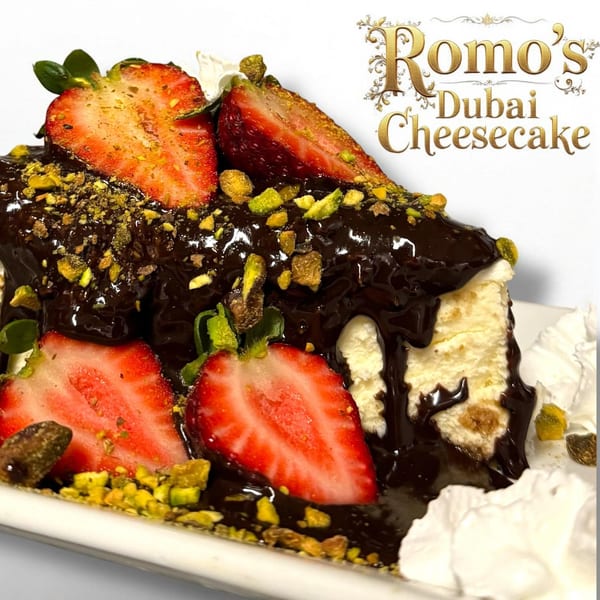 A slice of Romo's Dubai Cheesecake, topped with chocolate, strawberries, pistachios, and whipped cream.