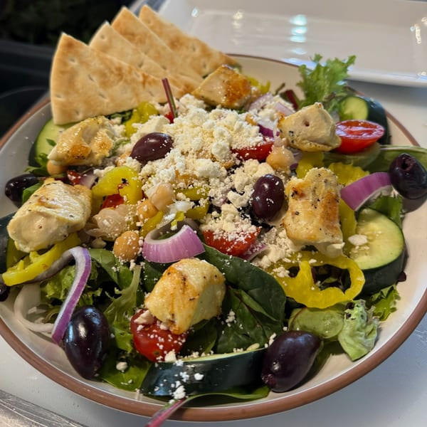 A vibrant Mediterranean salad with grilled chicken, feta, olives, and pita bread.