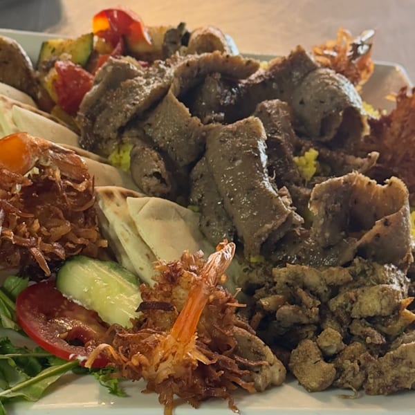 A large platter of Romo's Mediterranean Grill's gyro meat, chicken, vegetables, and pita bread.