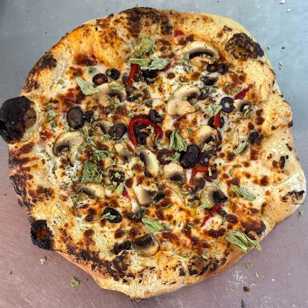 A freshly baked Mediterranean pizza with mushrooms, olives, red peppers, and herbs.