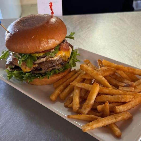 A large burger with cheese, bacon, and lettuce, served with a side of golden french fries.